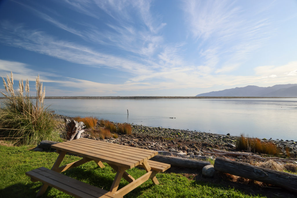 Image of toetoe grass and a picnic table sitting on the edge of Lake Ferry 